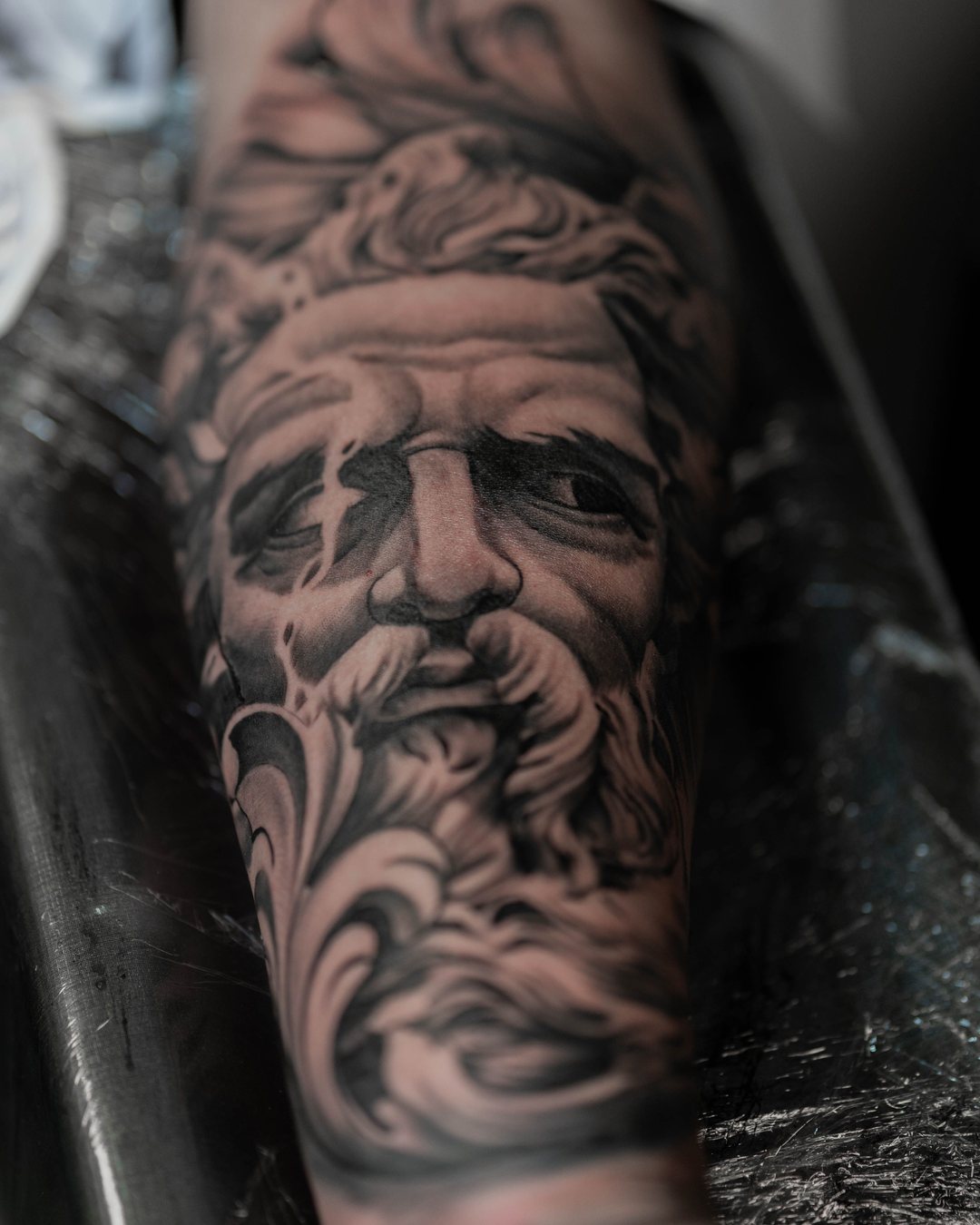 Rostro de Zeus en realismo black y grey en el antebrazo