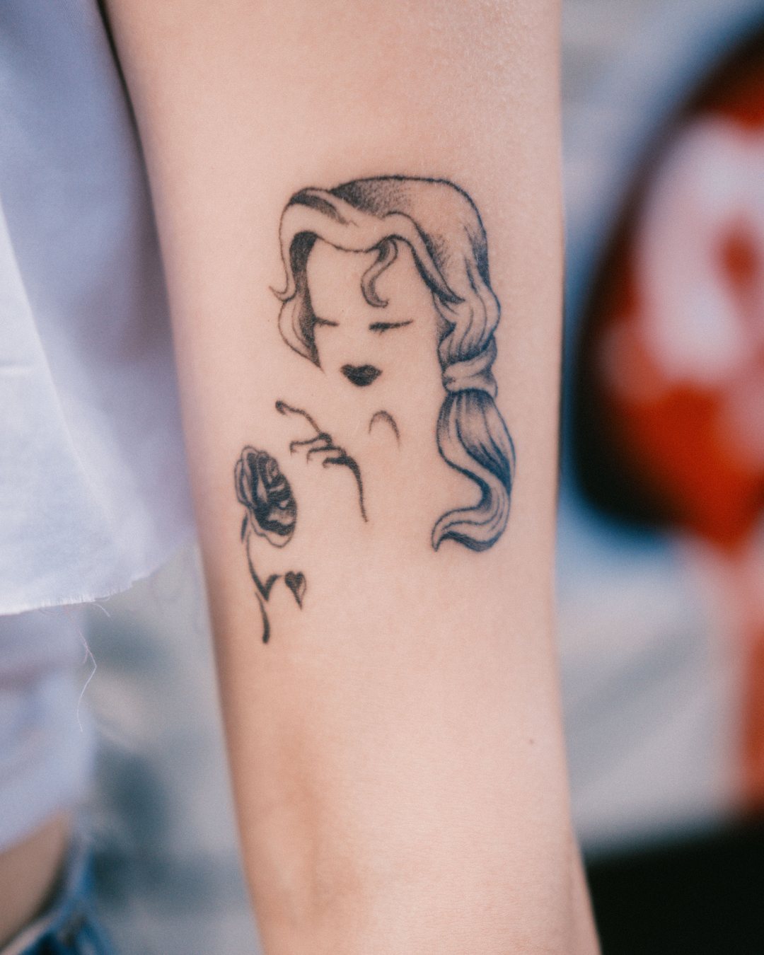 Retrato de mujer con una rosa en fine line en el antebrazo